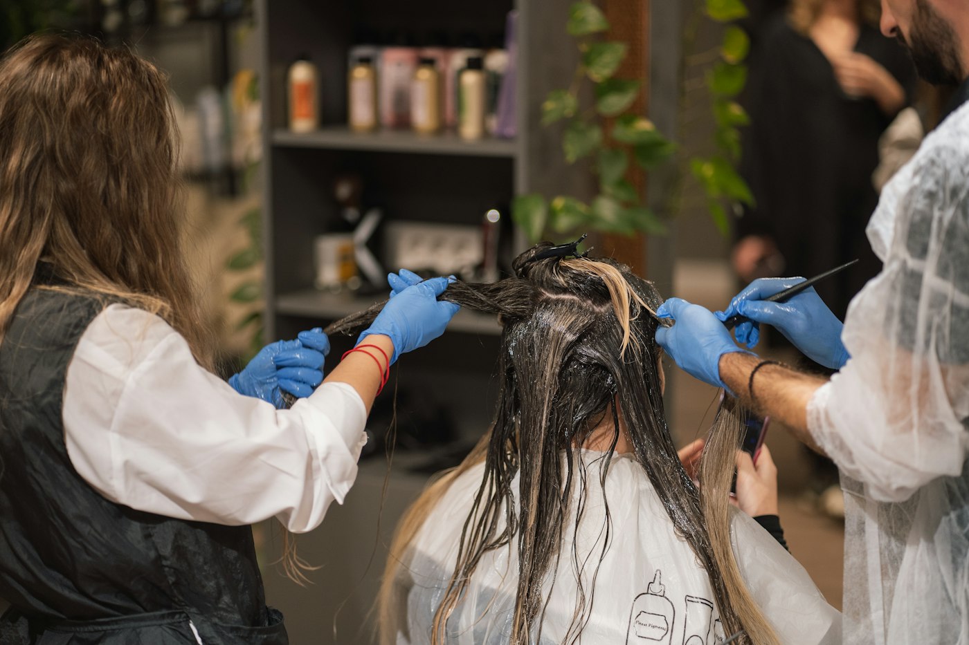 Dos coloristas con guantes aplican tinte con pincel sobre el cabello de una clienta