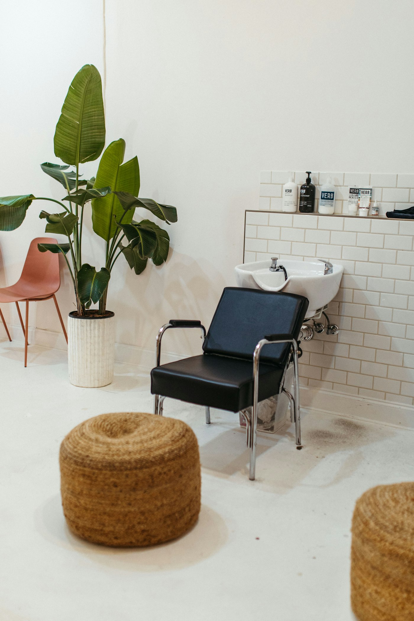 Lavacabezas negro junto a una pared de azulejo blanco y una planta
